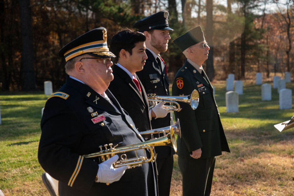 Four buglers stand in a row in a cemetery.